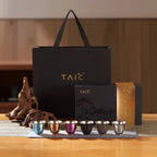 Pure titanium tea cup gift set — six anodized cups in a row beside branded gift bag and landscape box on tea table
