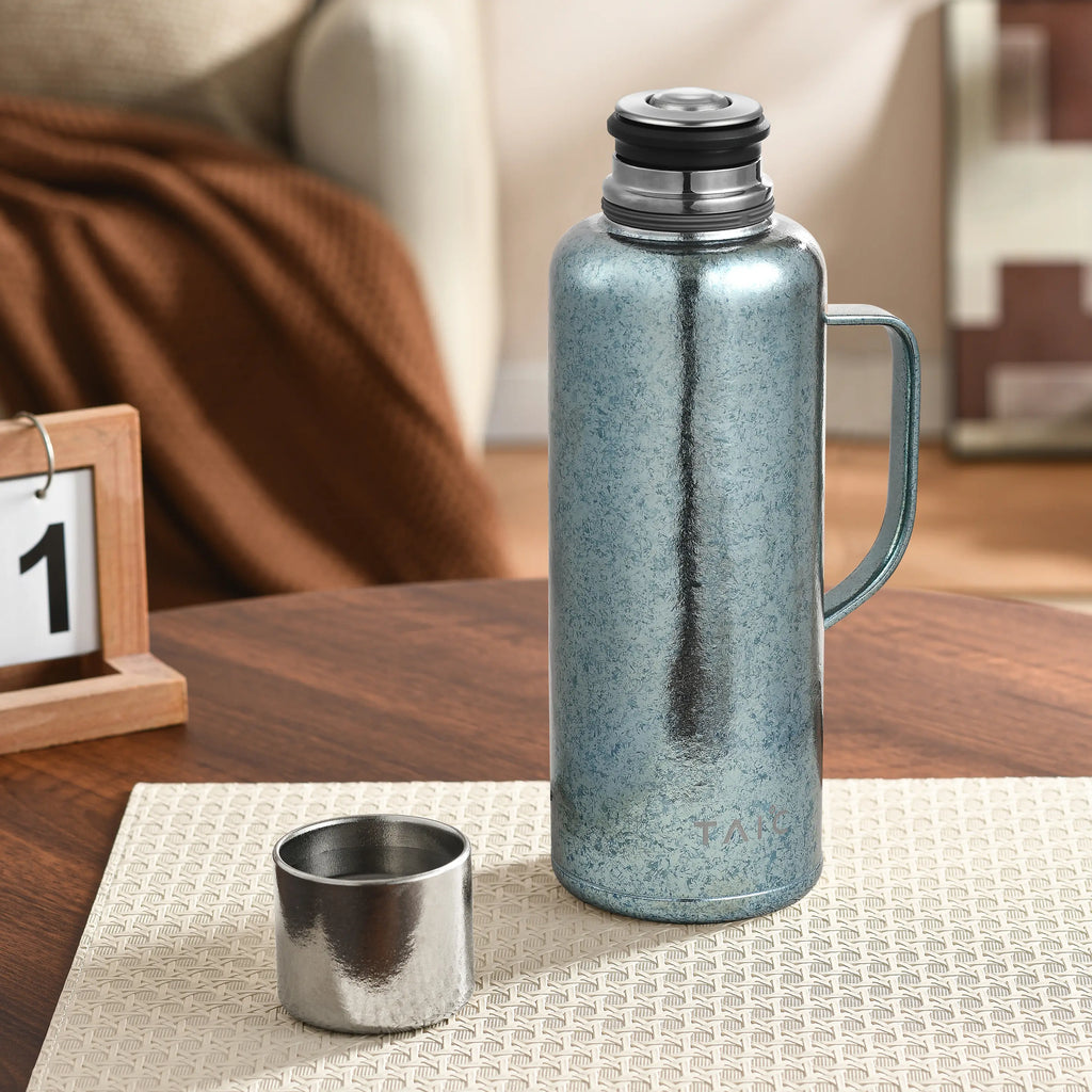 Frosted ice-blue titanium thermal carafe on table beside detached cup, temperature plug seated on top