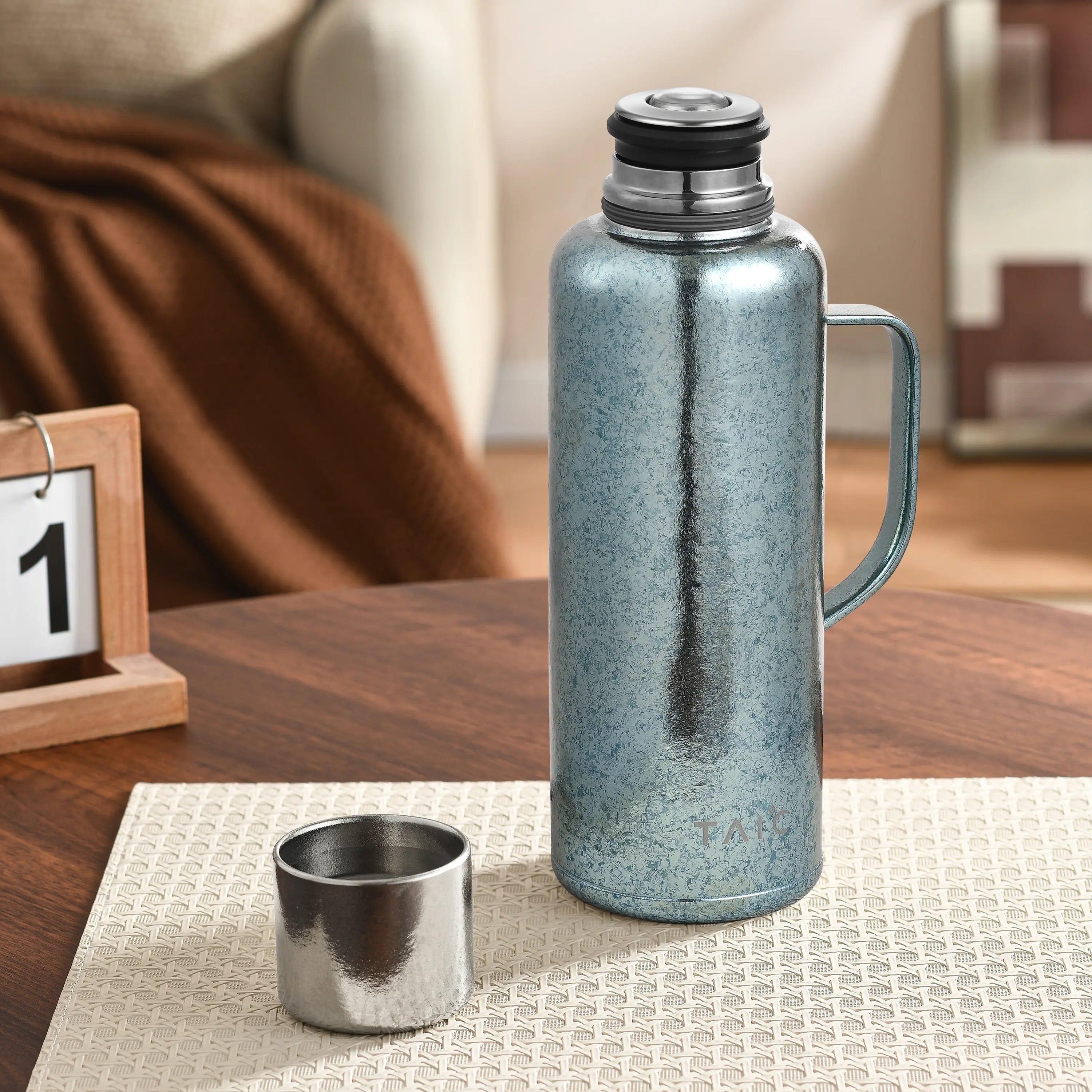 Frosted ice-blue titanium thermal carafe on table beside detached cup, temperature plug seated on top