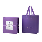Titanium tumbler gift box closed with iris illustration card beside matching purple TAIC carry bag, packaging view