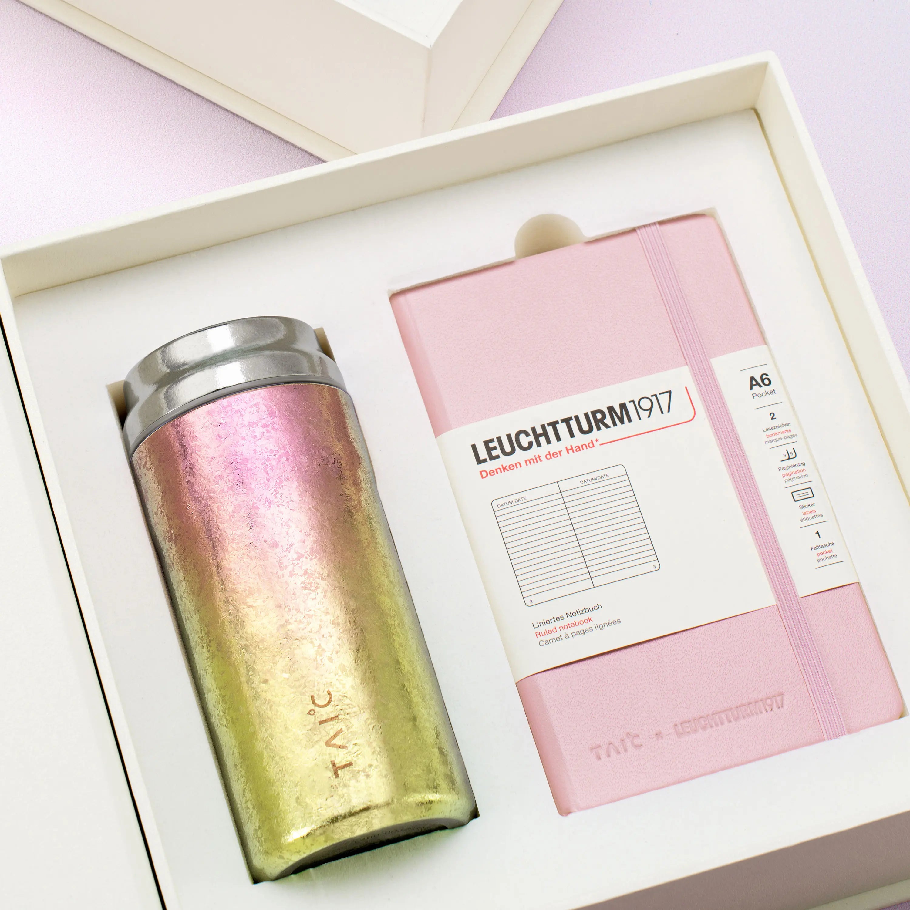 Совместный подарочный набор TAIC x LEUCHTTURM1917 — коробочный розовый ежедневник рядом с розово-золотым градиентным стаканом