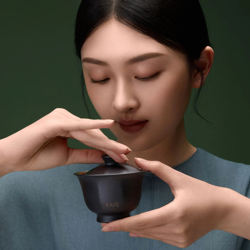 Pure titanium travel tea set gaiwan held to the face, woman inhaling aroma from matte black lidded bowl