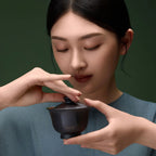 Pure titanium travel tea set gaiwan held to the face, woman inhaling aroma from matte black lidded bowl