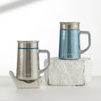 Pure titanium office mugs in silver and blue aurora finishes styled on stone blocks, lifestyle shot
