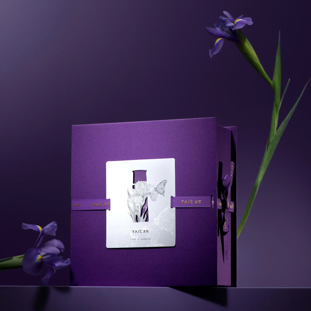 Closed purple titanium tumbler gift box with silver iris-and-butterfly cutout card and ribbon bow, single iris stem