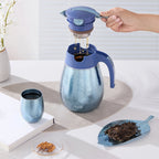 Blue titanium 1L thermal carafe with a hand lifting the tea filter, brewed tea dripping in beside a cup