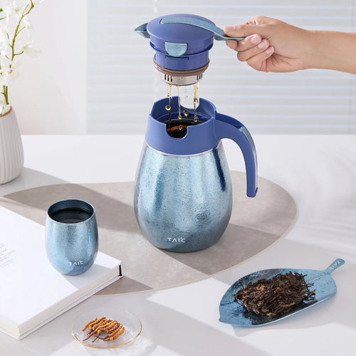 Blue titanium 1L thermal carafe with a hand lifting the tea filter, brewed tea dripping in beside a cup