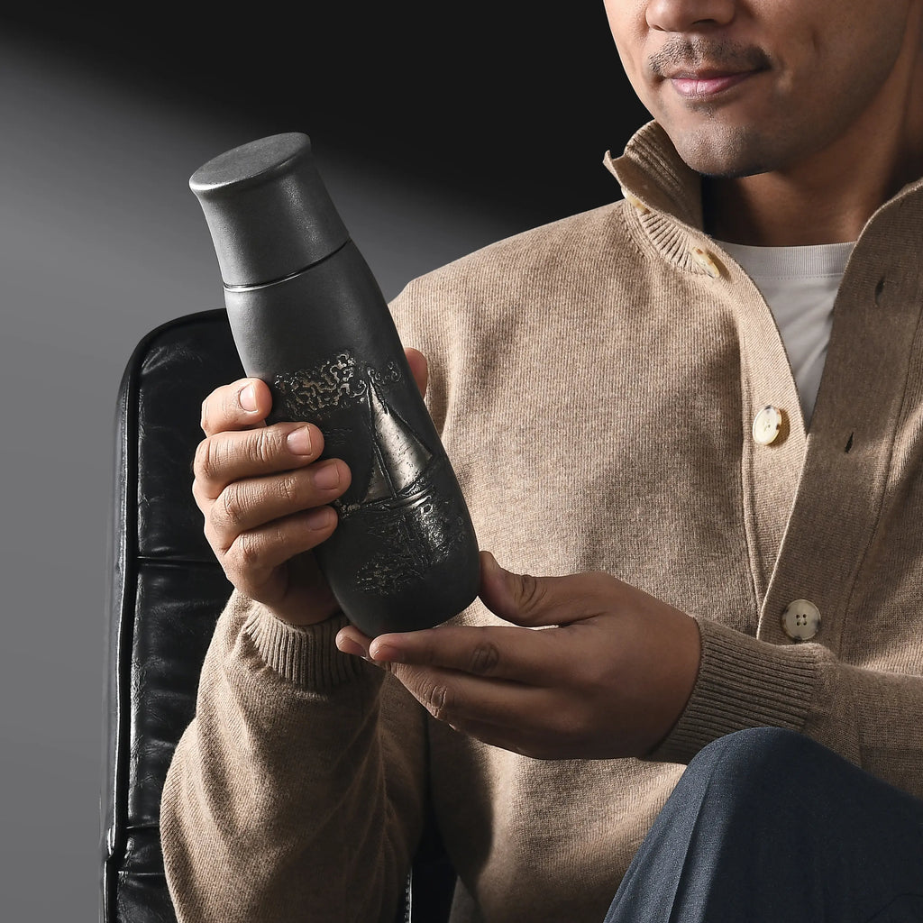 Monet Sailboat pure titanium infuser tumbler in charcoal finish, held by a smiling man in a tan cardigan