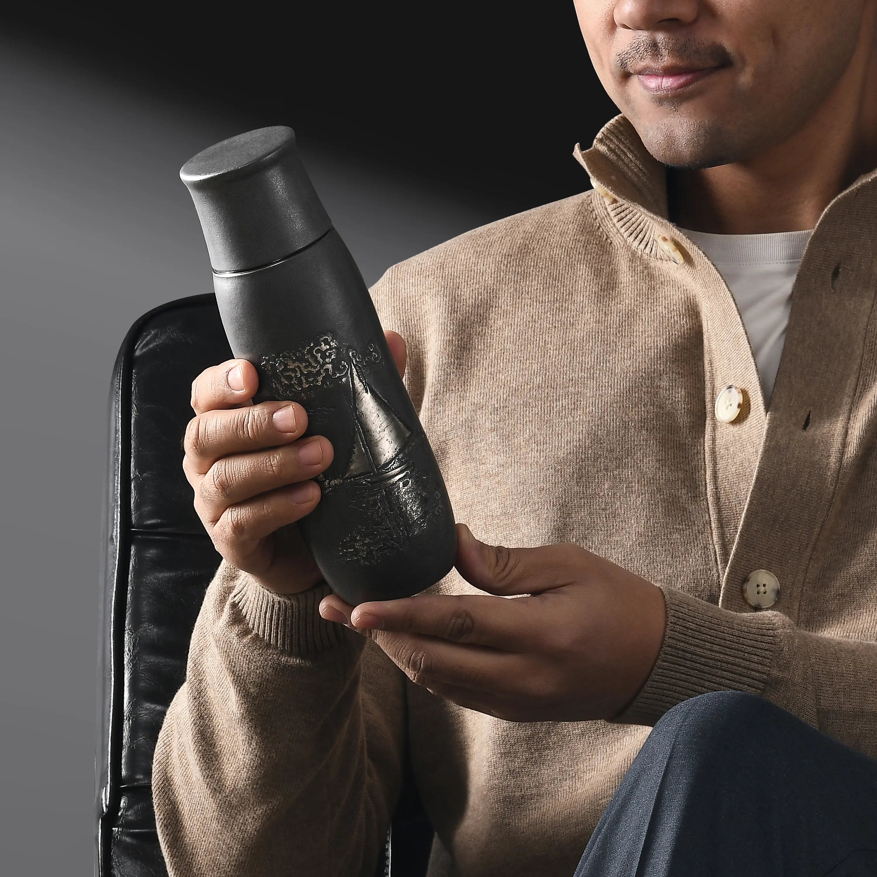 Monet Sailboat pure titanium infuser tumbler in charcoal finish, held by a smiling man in a tan cardigan
