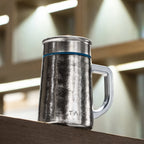 Pure titanium office mug 450mL in natural finish with blue band on a wooden ledge in a blurred cafe