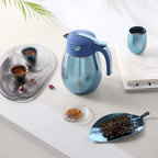 Overhead flatlay of a blue speckled titanium thermal carafe with matching cup, tea cups and leaf tray