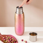 Finger pressing the push-button plug of rose-gold Aurora titanium tea infuser tumbler, dried rosebuds nearby