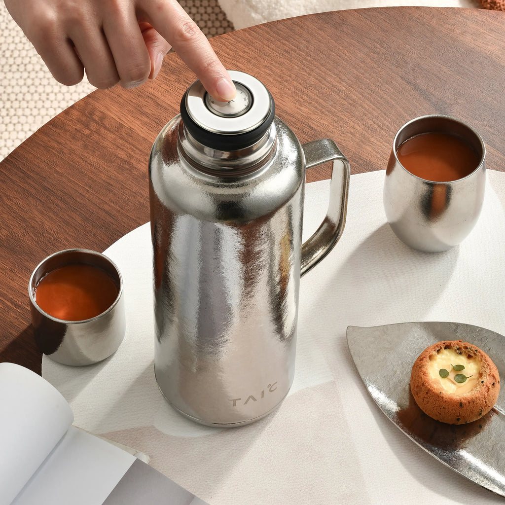 Pure titanium thermal carafe with finger pressing temperature dial on lid, poured tea in two cups overhead