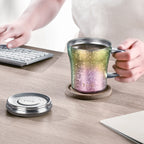 Iridescent green-to-pink titanium mug on a coaster at a keyboard desk, lid set aside