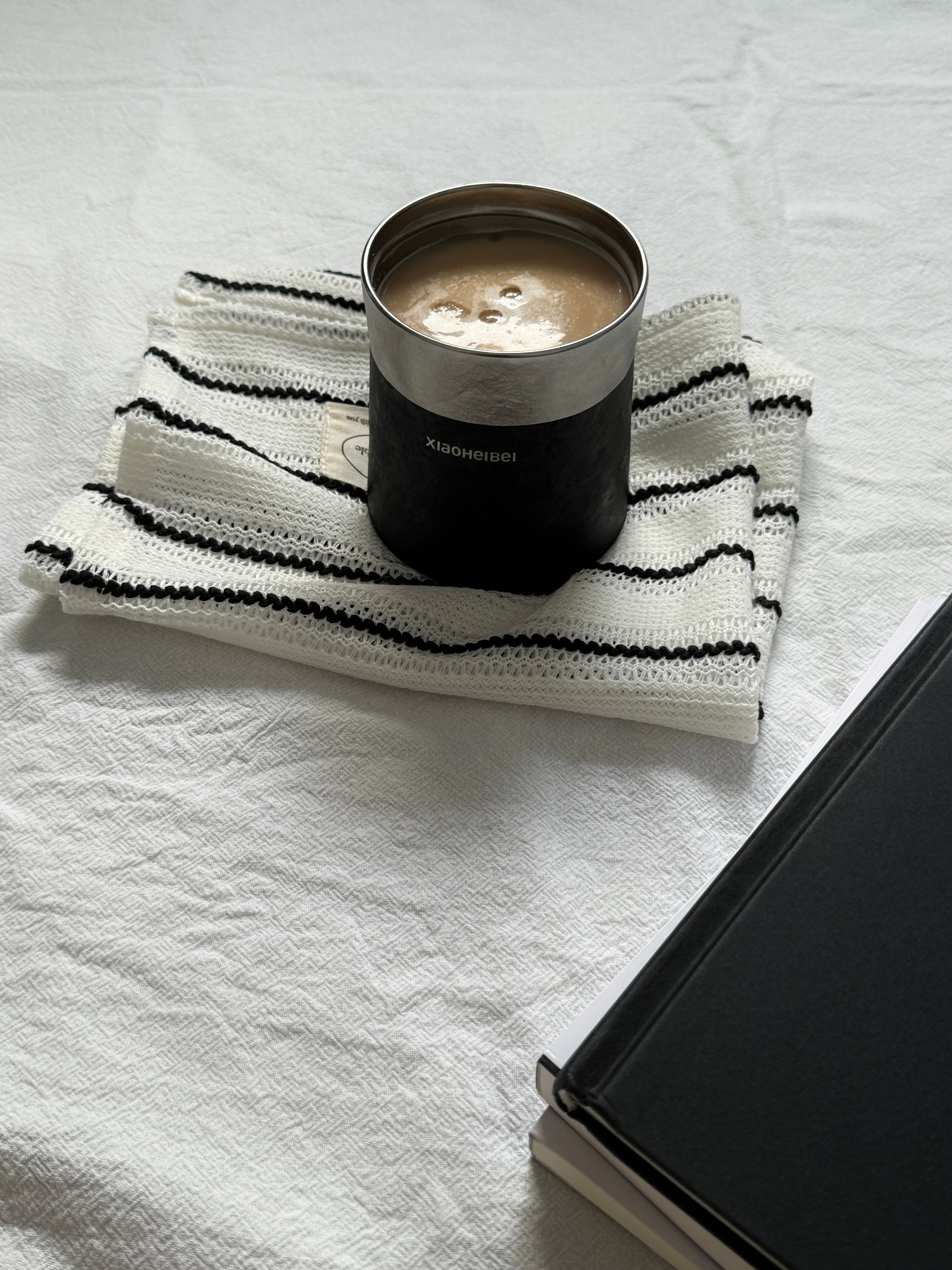 Кофейная кружка BlackInTi из чистого титана — крышка снята, наполнена латте, стоит на полосатой ткани