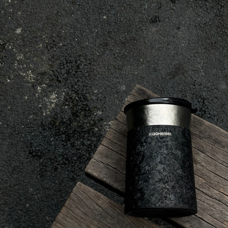 Кофейная кружка BlackInTi из чистого титана — кружка лежит на состаренной деревянной доске над тёмным камнем